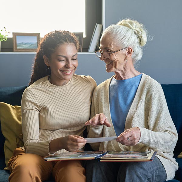 stock-photo-happy-old-woman-looking-at-her-granddaughter-while-showing-her-family-photos-2323337737 young woman helping senior woman